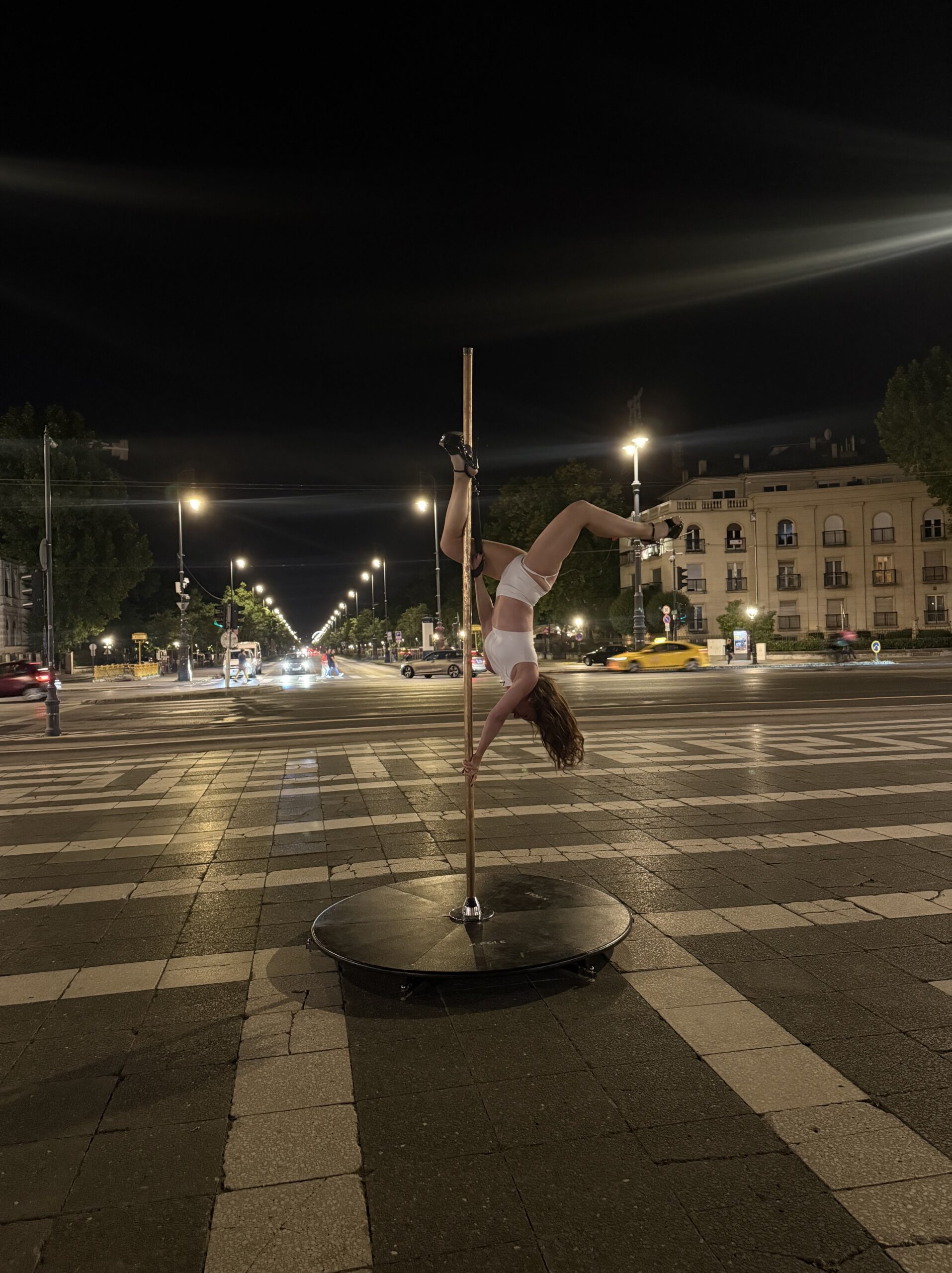 Éjszakai rúdtánc Budapest egyik sugárútján, fényfolyamokkal és autók mozgásával